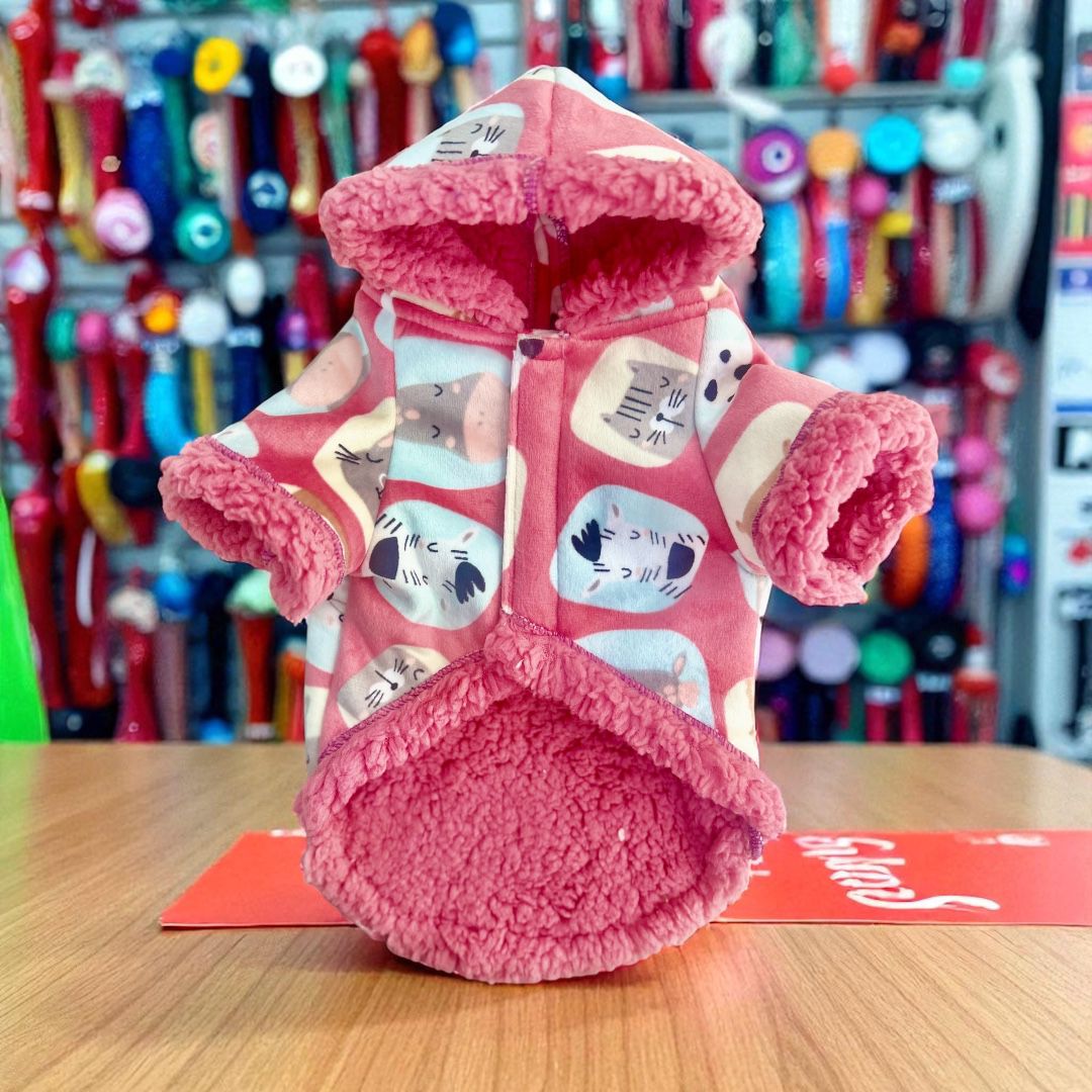 Chaqueta rosa decorada con capucha colocada sobre mesa con fondo de tienda.