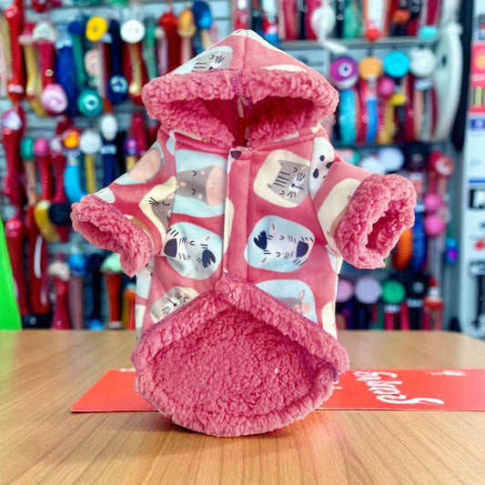 Chaqueta rosa decorada con capucha colocada sobre mesa con fondo de tienda.