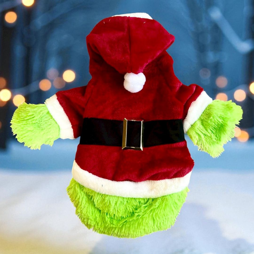 Disfraz Grinch navideño para perro con abrigo rojo y peluche verde, fondo invernal con luces cálidas.

