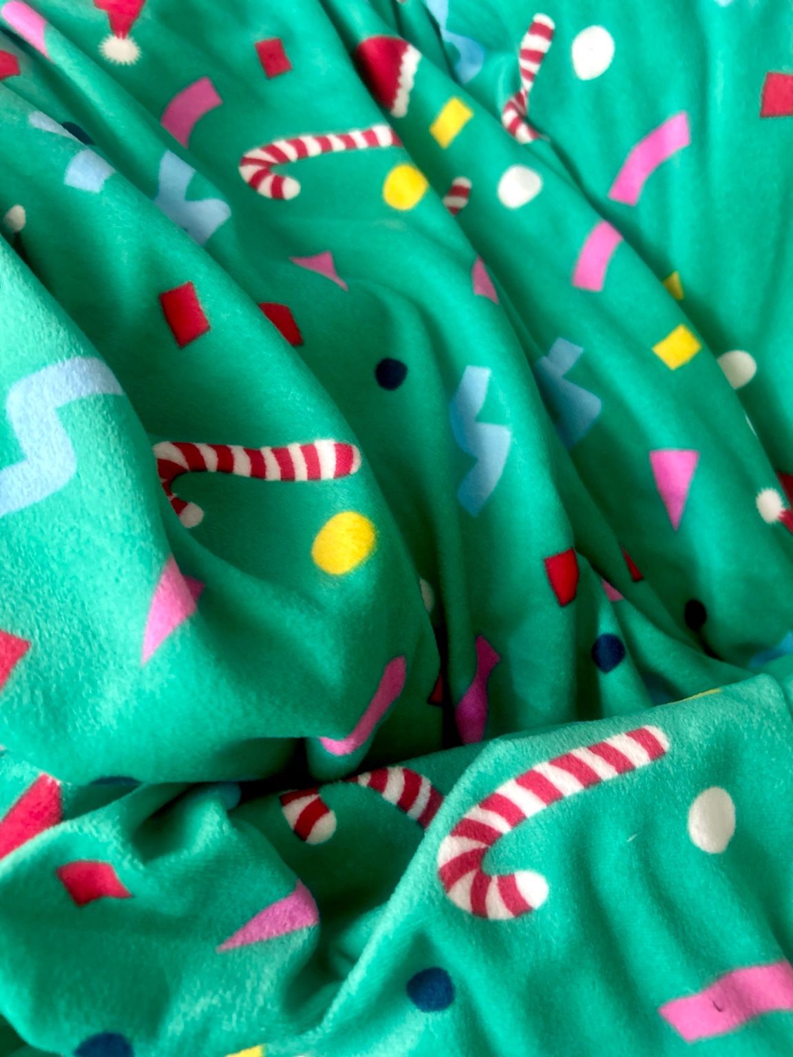 Primer plano de tela verde con estampado navideño de bastones de caramelo y copos de nieve del disfraz de perro