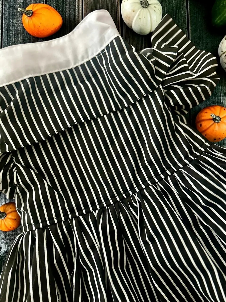 Detalle del disfraz de Jackie para perrita, con tela de rayas negras y blancas, cuello blanco y diseño inspirado en El extraño mundo de Jack, acompañado de elementos decorativos de Halloween.
